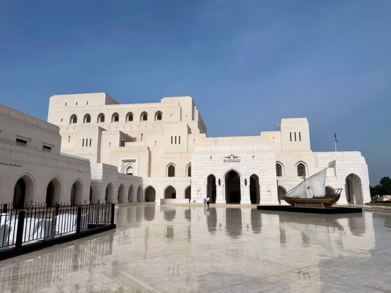 Royal opera house muscat w omanie, jasny gmach z arkadami i łodzią na dziedzińcu po deszczu