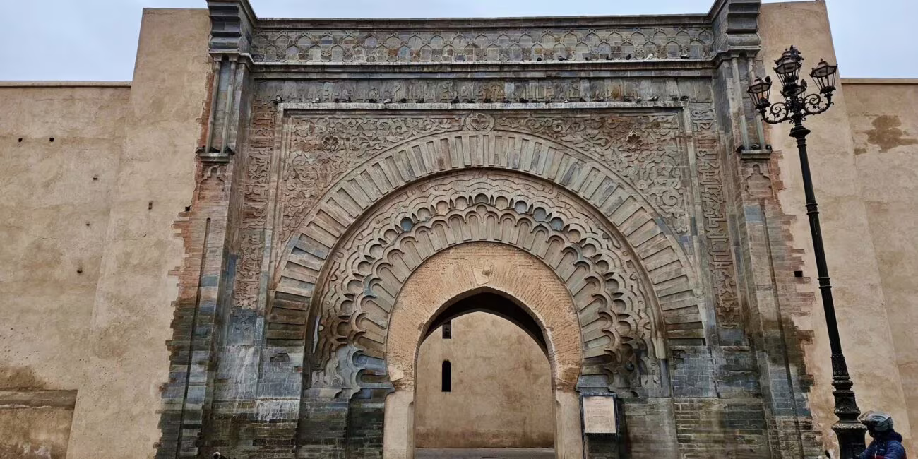 Zabytkowa, bogato zdobiona kamienna brama z łukiem i łagodnymi wykończeniami, na tle ulicy i lampy.