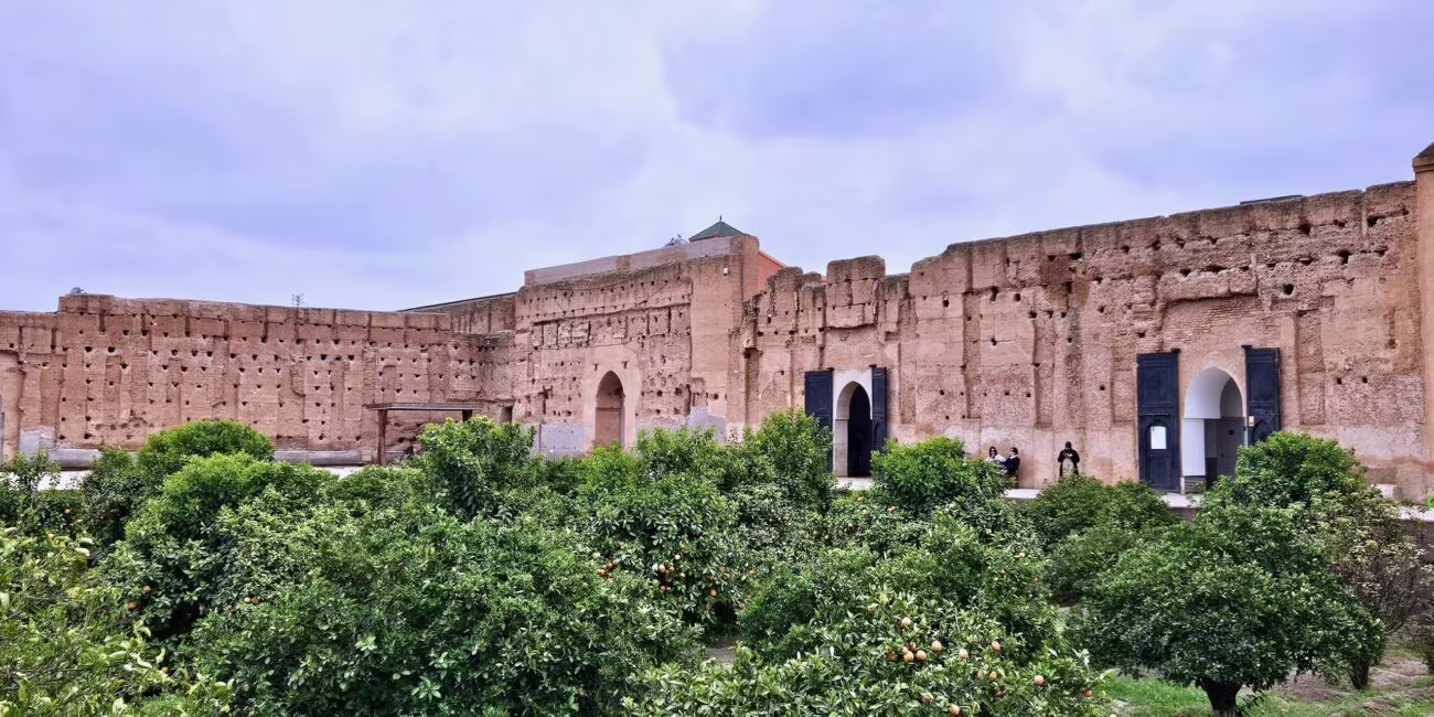 Forty starożytne mury z cegły otaczają ogród z drzewami owocowymi i dwoma wejściami z łukami; grupa osób siedzi przy ścianie.