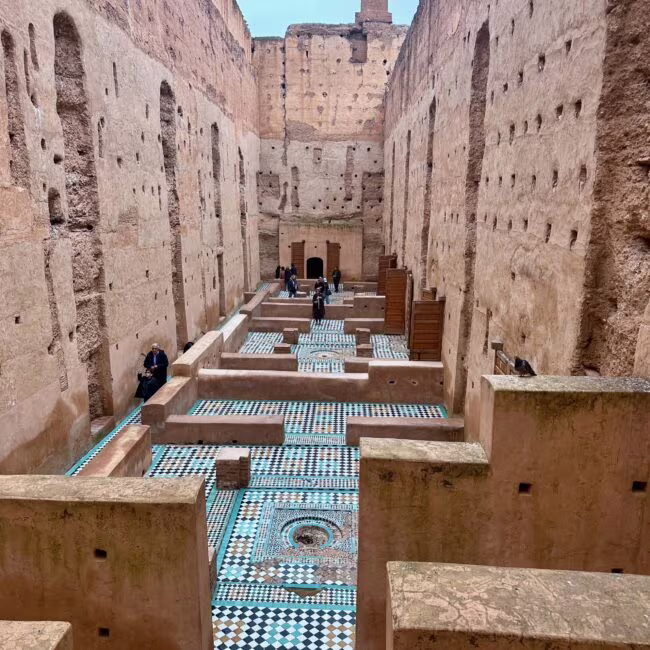 Wnętrze starożytnego adaptowanego dziedzińca z wysokimi, surowymi murami obronnymi, ozdobionymi licznymi otworami, u dołu kolorowe mozaikowe podłogi i schodkowe przejścia.