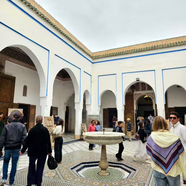 Ogromny dziedziniec w stylu mauretańskim, kolorowy mozaikowy podłogowy okrąg fontanną w centralnym punkcie, otoczony białymi arkami i zwiedzającymi.