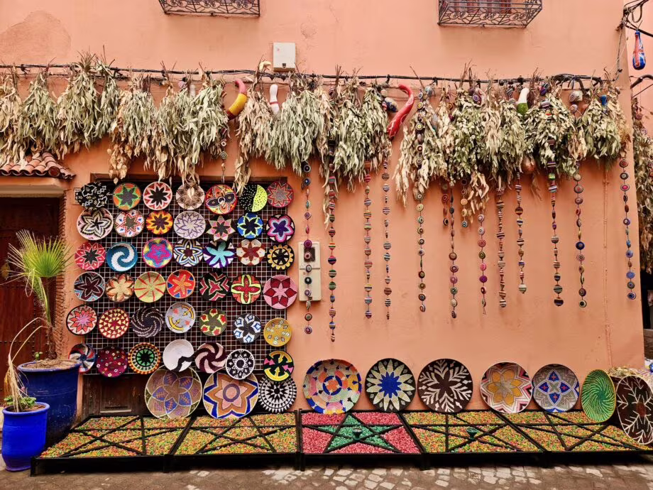 Krajobraz sklepowy z suszonymi ziołami na górze i wisienkami kolczykami; na dole kolorowe plecione miski i dekoracyjne płaskie talerze, na tle ceglanej ściany.