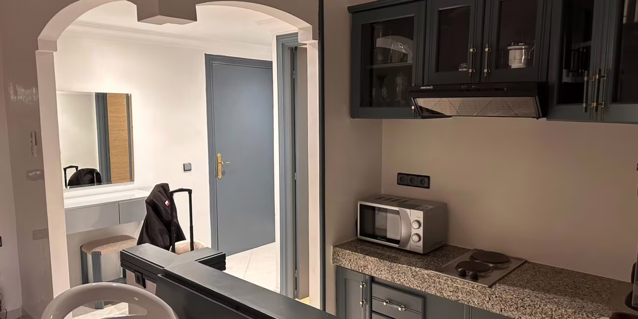 Kuchnia z szafkami w odcieniu granatowym, blatami granitowymi, mikrofalówką i kuchenką elektryczną; widok na wejście z arkadowym przejściem i lustrem w przedpokoju.