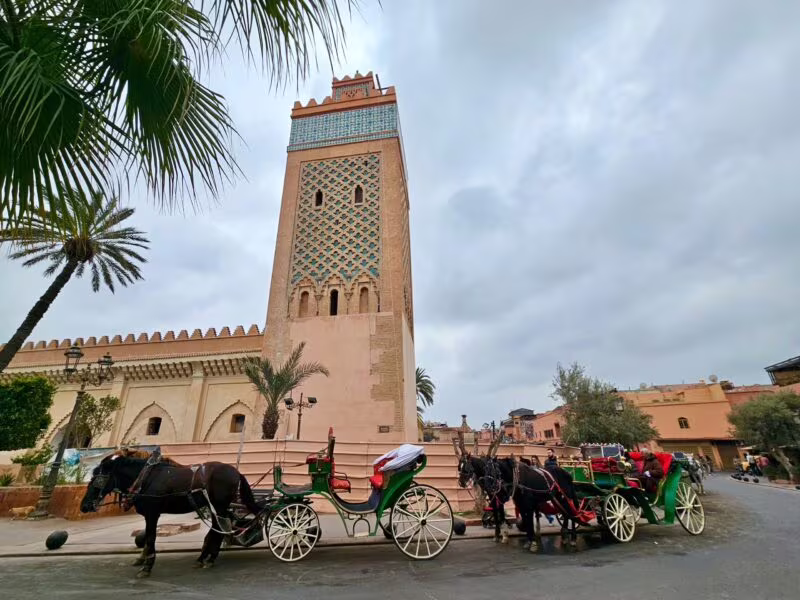 Bab al qsar w marrakeszu, wysoka wieża z dekoracyjną fasadą i konne dorożki na ulicy.