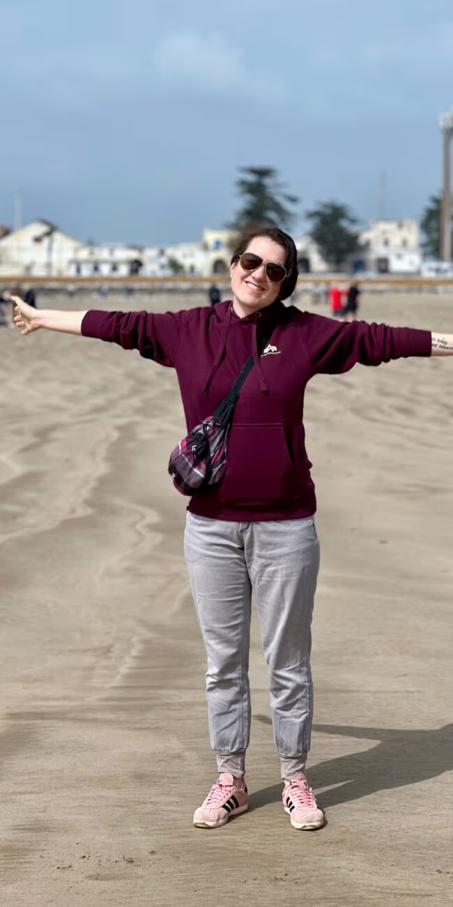 Essaouira, maroko: plaża w mieście, kobieta uśmiechnięta z rozłożonymi rękami na piasku