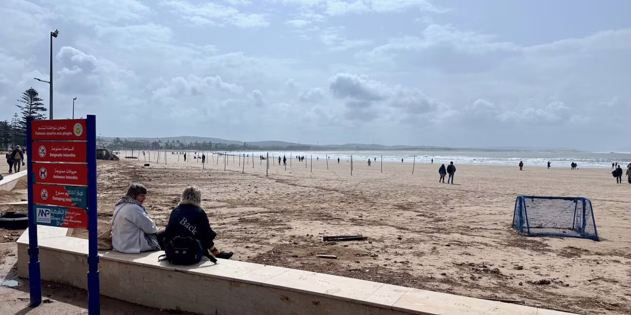 Plaża w mieście essaouira w maroku, ludzie spacerują przy brzegu i przyboju pod chmurami