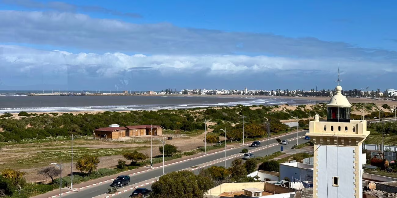 Widok z hotelu na plażę w essaouirze: ocean, promenada i białe minaretowe wieżyczki w tle miasta