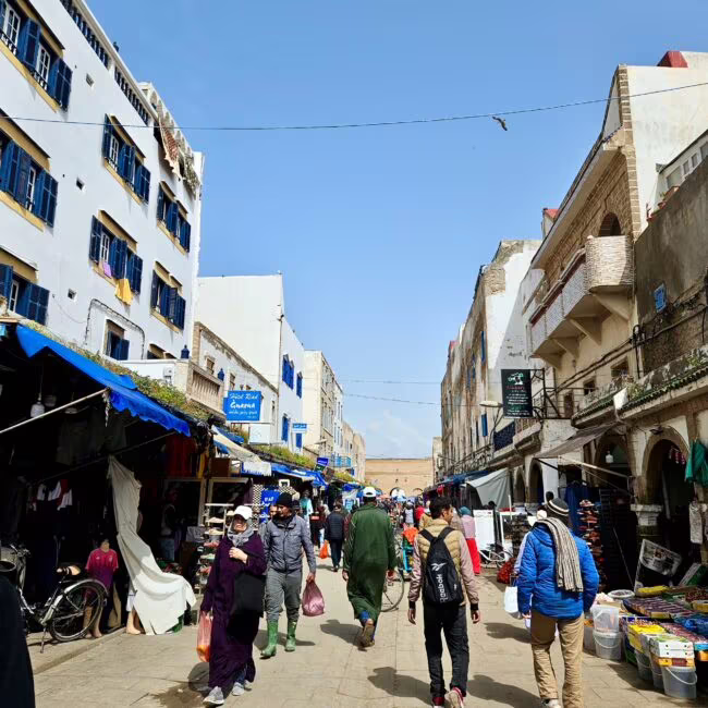 Essaoira mellah w maroku, targ uliczny z przechodniami między białymi kamienicami i niebieskimi okiennicami