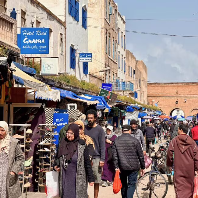 Maroko, essaouira: mellah, ulica pełna ludzi i stragany pod błękitnymi banerami hoteli
