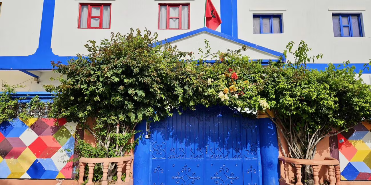 Morocco essaouira: szkolny budynek z niebieskimi drzwiami i flagą na tle zielonych krzewów