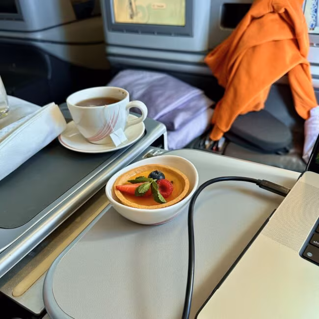 Posiłek w biznes klasie air china: filiżanka herbaty i tarta owocowa na rozkładanym stoliku przy fotelu